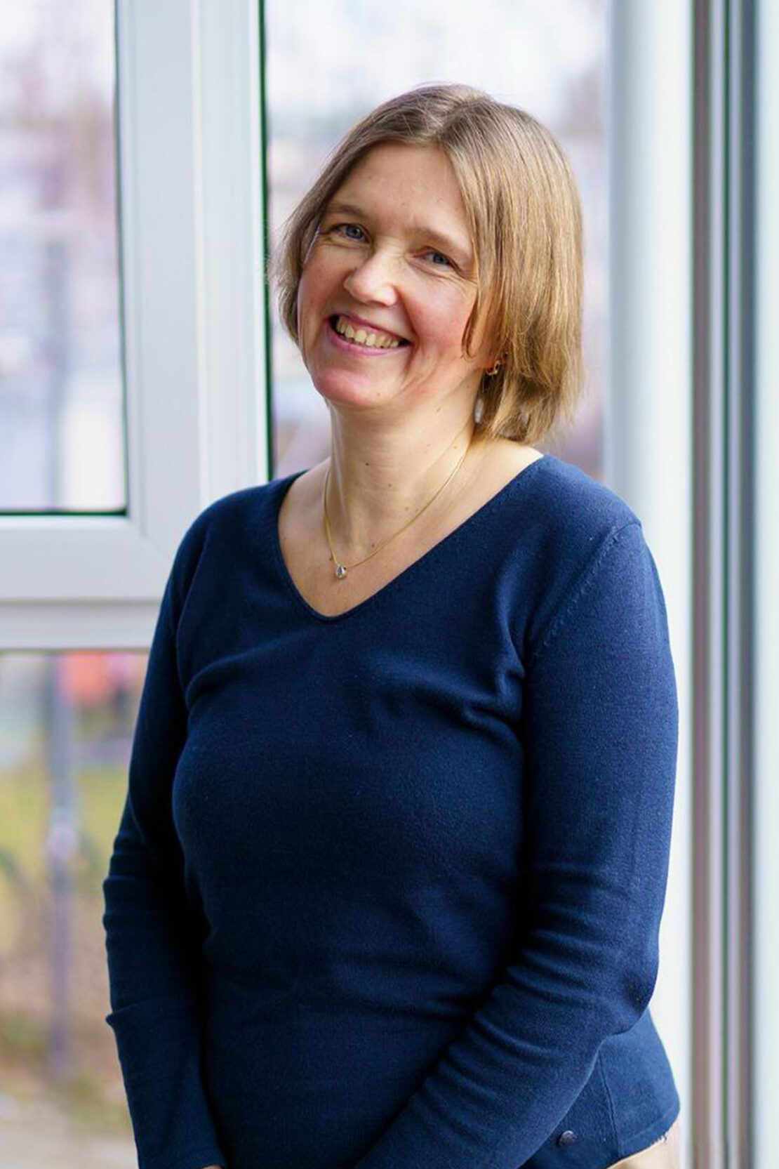 Sandra Oldenburg, Rechtsanwalts- und Notarfachangestellte der Ebert Rechtsanwälte in Kiel steht am Fenster und lächelt.
